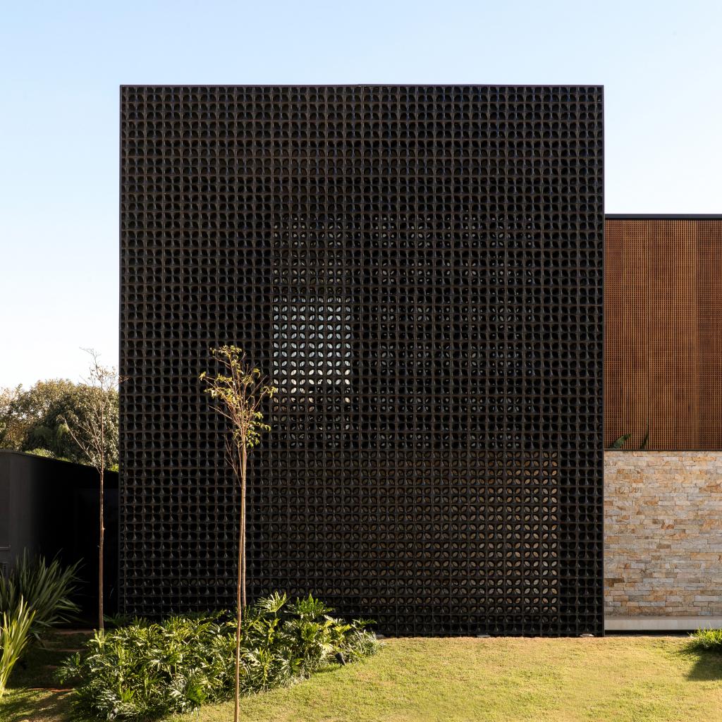 Перфорированные блоки, черные кирпичи, древесина и камень покрывают дом, состоящий из трех частей: фото
