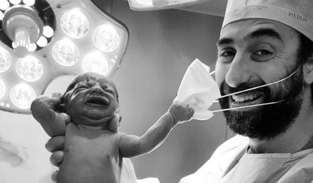 Символом надежды назвали фотографию новорожденного младенца, пытающегося снять маску с лица врача