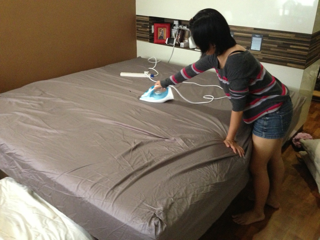 женщина гладит белье на кровати