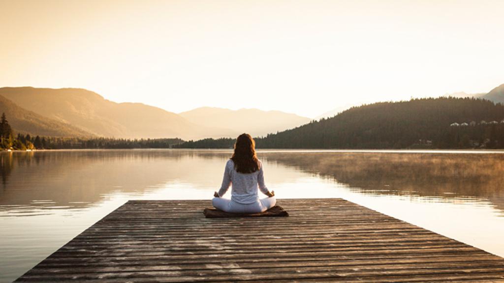 Женщина медитирует на берегу озера