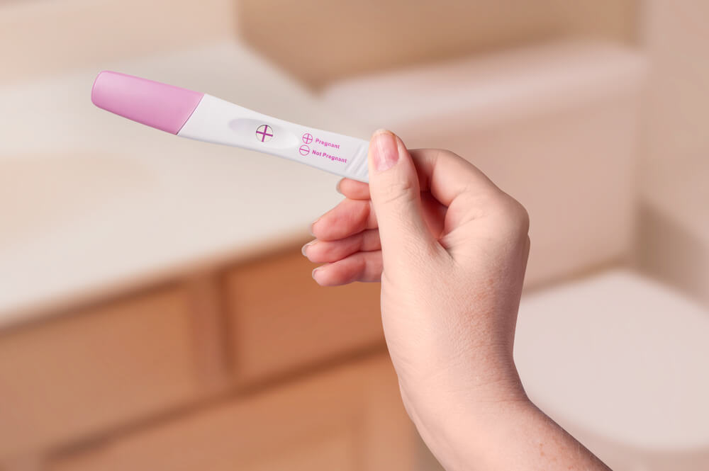 Фото теста на беременность с двумя полосками в руке у девушки с красивым маникюром