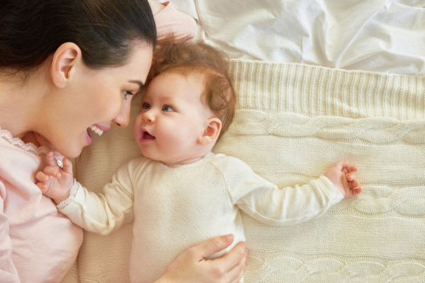 mother smiles at baby lying on bed