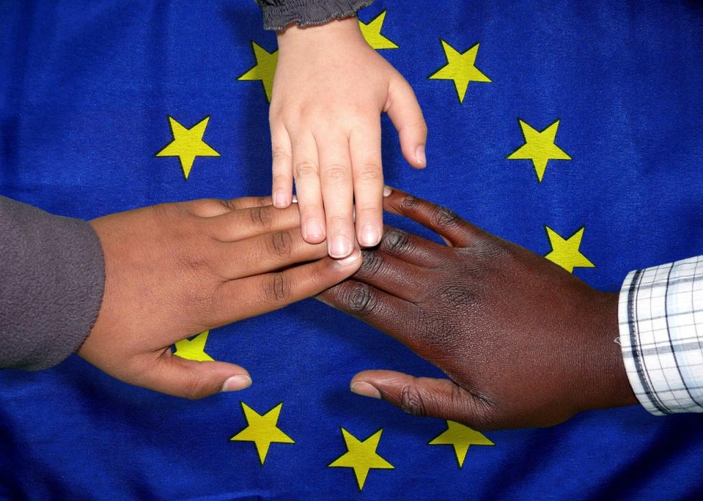руки людей разных национальностей на фоне флага Евросоюза